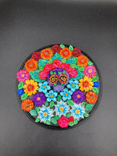 Load image into Gallery viewer, Frida Kahlo inspired calavera with a black wood frame, this Day of the Dead wall decor piece is perfect for adding a traditional Mexican folk art touch to any home. Add a unique touch of style to your home with this intricately detailed, Frida Kahlo-inspired calavera clay wall art. The design features an eye-catching crown of flowers, plus a vibrant bouquet, perfect for any Day of the Dead celebration. Bring a bright and colorful piece of art to your home with this stunning wall hanging.