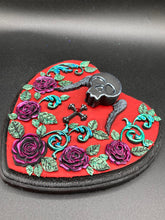 Load image into Gallery viewer, This Memento Mori Wall Art Decor is a one-of-a-kind art piece, skillfully crafted with a black polymer clay skull and wings on a dark red wood frame, decoratively woven with dark red roses and vines. It's perfect for adding an eye-catching touch to any wall and makes a unique, bold gift. Measurements: H 6 3/4" x W 7” x D 1 1/2"