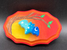 Load image into Gallery viewer, This unique Starry Night Mini Bat Wall Art Decor is hand sculpted and painted in vivid hues to offer an eye-catching decoration for your living space. The bat is painted in a gradient of light to dark blue, and is complemented by white stars and a crescent moon. The wood frame is painted in yellow, orange and red for a stunning sundown effect for a drastic contrast to the blue bat.