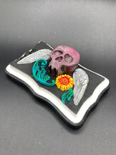 Load image into Gallery viewer, This unique wall art decor, crafted with hand-molded polymere clay and painted on a wooden frame, brings to life a classic Dia De Los Muertos Calavera with its fiery-red skull and bright yellow-orange flower and vine accents. Perfect for accenting your crystal display, witchy altar, or indoor garden.