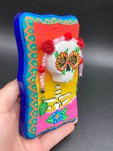 Load image into Gallery viewer, Transform your walls with this handcrafted polymer clay wall art. Showcasing a vibrant Frida Kahlo inspired calavera with hand-beaded floral crown, this Day of the Dead wall decor piece is perfect for adding a traditional Mexican folk art touch to any home.