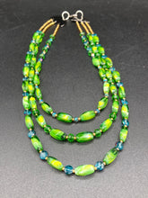 Load image into Gallery viewer, This adjustable glass beaded necklace features a combination of vivid green, blue, and gold hues and a mixture of shapes, creating an eye-catching spectrum of colors and a complex look. The rectangular green glass beads form the predominant part of the three-strand piece, which offers a bold and elegant fashion statement that is ideal for the Spring season. Measurements: Necklace is 17” in length, can be adjusted up to 19" in length