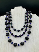Load image into Gallery viewer, This Bohemian style necklace is composed of three strands of shimmery large black and dark purple glass beads, along with floral metal beads. The elegant drape creates a bold and fierce look that is ideal for a variety of occasions, such as cocktail chic attire and weddings. It is a perfect minimalist accessory.  Measurements:  Necklace is 16” in length - adjustable to 18"