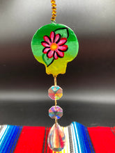 Load image into Gallery viewer, Nature inspired hand crafted polymer clay skull is painted in ombre colors from dark green to light yellow and decorated with flowers on back and over eyes. Light gold glass beaded chain with iridescent crystals. A perfect hanging Day of the Dead art piece to add to your ofrenda, hang next to your display of crystals or witchy altar, add to your skull collection or hang as an art piece on the wall or near a window. Measurements: H 1 1/2” x W 1 1/2” x D 3/4”
