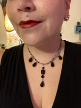 Load image into Gallery viewer, This adjustable collar-style necklace features silver and black glass beads in a combination of both teardrop and rectangular shapes, designed to create visual complexity and depth. The two strands are held together with two-hole silver and black beads, creating a stunningly bold and elegant draped collar that enhances any outfit.