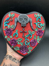Load image into Gallery viewer, This Memento Mori Wall Art Decor is a one-of-a-kind art piece, skillfully crafted with a black polymer clay skull and wings on a dark red wood frame, decoratively woven with dark red roses and vines. It's perfect for adding an eye-catching touch to any wall and makes a unique, bold gift. Measurements: H 6 3/4" x W 7” x D 1 1/2"