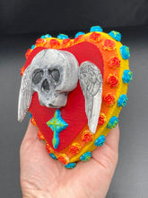 Load image into Gallery viewer, This Memento Mori Wall Art Decor is a unique statement piece to add a pop of color to your walls. Handcrafted with black and white polymer clay, acrylic paint, and a wood frame, the skull artwork is decorated with small turquoise and yellow-orange flowers and a turquoise and gold cross. Perfect for a Day of the Dead altar or a witchy home decor display.