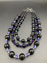 Load image into Gallery viewer, This Bohemian style necklace is composed of three strands of shimmery large black and dark purple glass beads, along with floral metal beads. The elegant drape creates a bold and fierce look that is ideal for a variety of occasions, such as cocktail chic attire and weddings. It is a perfect minimalist accessory.  Measurements:  Necklace is 16” in length - adjustable to 18"