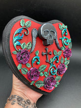 Load image into Gallery viewer, This Memento Mori Wall Art Decor is a one-of-a-kind art piece, skillfully crafted with a black polymer clay skull and wings on a dark red wood frame, decoratively woven with dark red roses and vines. It's perfect for adding an eye-catching touch to any wall and makes a unique, bold gift. Measurements: H 6 3/4" x W 7” x D 1 1/2"