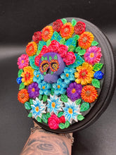 Load image into Gallery viewer, Frida Kahlo inspired calavera with a black wood frame, this Day of the Dead wall decor piece is perfect for adding a traditional Mexican folk art touch to any home. Add a unique touch of style to your home with this intricately detailed, Frida Kahlo-inspired calavera clay wall art. The design features an eye-catching crown of flowers, plus a vibrant bouquet, perfect for any Day of the Dead celebration. Bring a bright and colorful piece of art to your home with this stunning wall hanging.