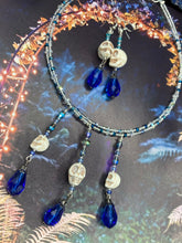 Load image into Gallery viewer, This adjustable collar-style necklace features two shimmery strands of silver and blue glass beads, with three skull charms boasting large, luminous blue teardrop glass beads adding extra shimmer and movement. Measurements: Necklace is 14 3/8” adjustable up to 18" in length