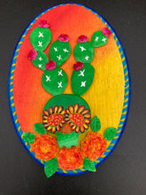 Load image into Gallery viewer, This handcrafted polymer clay wall art features a wood frame painted in a gradient from light yellow to dark red, creating a stunning sunset look. With a bright green skull cactus plant and bright pink blooming flowers. Boasting vivid marigold blooms and a deep royal blue frame to make a bold contrast with the warm background hue. this piece is sure to make a statement. Measurements: H 7" x W 5” x D 1 1/2"
