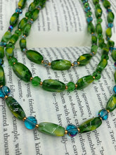 Load image into Gallery viewer, This adjustable glass beaded necklace features a combination of vivid green, blue, and gold hues and a mixture of shapes, creating an eye-catching spectrum of colors and a complex look. The rectangular green glass beads form the predominant part of the three-strand piece, which offers a bold and elegant fashion statement that is ideal for the Spring season. Measurements: Necklace is 17” in length, can be adjusted up to 19" in length
