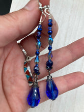 Load image into Gallery viewer, This stunning, one of a kind pair of celestial beaded earrings is a bold addition to any jewelry collection. Crafted with vibrant blue glass beads, the color contains varied shades of blue, purple, and hints of gold to create unique texture. The design is inspired by the awe-inspiring beauty of the majestic galaxy. Measurements: 2 3/4 ” in length