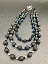 Load image into Gallery viewer, This statement piece features 3 long strands of flat matte black and dark blue glass beads, complemented by a floral metal beaded necklace. It gracefully drapes across the neck for a fierce, yet elegant look, making it perfect for cocktail chic attire, weddings, or minimalist styling.  Measurements:    Necklace is 16” in length - adjustable to 18"
