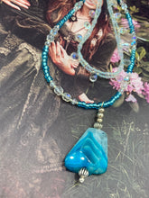 Load image into Gallery viewer, This exquisite necklace features a vibrant Sea Blue Agate Natural Stone Pendant and two strands of multi-colored glass beaded necklace. An adjustable collar-style strand contains small, light blue beads and lots of iridescent double-hole beads for shimmer and sparkle. The longer strand features larger blue glass beads interspersed with clear and silver beads for a sophisticated, draped look. It's finished with a set of dainty matching earrings for a complete look. Necklace is 14”adjustable up to 18"