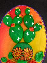 Load image into Gallery viewer, This handcrafted polymer clay wall art features a wood frame painted in a gradient from light yellow to dark red, creating a stunning sunset look. With a bright green skull cactus plant and bright yellow/red blooming flowers. Boasting vivid marigold blooms and a deep purple frame to make a bold contrast with the warm background hue. this piece is sure to make a statement. Measurements: H 7" x W 5” x D 1 1/2"