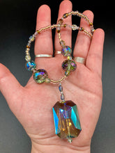 Load image into Gallery viewer, Make a bold statement with this shimmery aqua blue and gold tones glass beaded necklace. The large rectangular faceted shaped pendant creates a vivid contrast to the warm gold tones of the necklace, perfect for adding a rich pop of color to any Spring outfit. The draped design gives this piece an elegant, bohemian look. Measurements: Necklace is 20” in length,