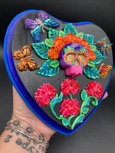 Load image into Gallery viewer, Frida Kahlo inspired calavera with a dark wood frame, this Day of the Dead wall decor piece is perfect for adding a traditional Mexican folk art touch to any home. Featuring an intricately detailed clay calavera in the style of Frida Kahlo, this Day of the Dead wall art decor is sure to be the centerpiece of any home décor. The calavera is wearing Frida's iconic crown of flowers and with several butterflies around her, ensuring it will bring both a unique and inspiring look to any wall.