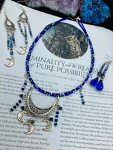 Load image into Gallery viewer, This stylish choker necklace showcases a large half moon pendant, adorned with glass beads and small, dangling crescent moon charms. Its eye-catching hues, of blue and silver, are complemented with delicate tints of purple and pink. Boasting an accentuated look and ample motion, this piece is sure to impress. Measurements: Necklace is 16 1/2”adjustable up to 18"