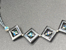Load image into Gallery viewer, This two-strand necklace, crafted from aqua-blue and silver toned glass beads, is a stunning statement piece. The addition of faceted triangle-shaped glass beads tucked between hematite square beads adds an exquisite and unique flair. The necklace gracefully drapes around the neck, bringing an air of bold and elegant flair to any ensemble it complements. 15” in length, can be extended up to 17"