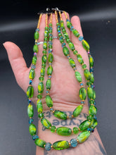 Load image into Gallery viewer, This adjustable glass beaded necklace features a combination of vivid green, blue, and gold hues and a mixture of shapes, creating an eye-catching spectrum of colors and a complex look. The rectangular green glass beads form the predominant part of the three-strand piece, which offers a bold and elegant fashion statement that is ideal for the Spring season. Measurements: Necklace is 17” in length, can be adjusted up to 19" in length