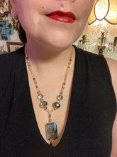 Load image into Gallery viewer, Make a bold statement with this shimmery aqua blue and gold tones glass beaded necklace. The large rectangular faceted shaped pendant creates a vivid contrast to the warm gold tones of the necklace, perfect for adding a rich pop of color to any Spring outfit. The draped design gives this piece an elegant, bohemian look. Measurements: Necklace is 20” in length,