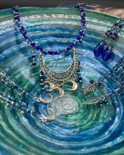 Load image into Gallery viewer, This stylish choker necklace showcases a large half moon pendant, adorned with glass beads and small, dangling crescent moon charms. Its eye-catching hues, of blue and silver, are complemented with delicate tints of purple and pink. Boasting an accentuated look and ample motion, this piece is sure to impress. Measurements: Necklace is 16 1/2”adjustable up to 18"
