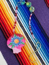 Load image into Gallery viewer, Nature inspired hand crafted polymer clay skull is painted in ombre colors from red, to light pink and decorated with flowers on back and over eyes. Three hearts rainbow hematite bead on forehead. Light pink glass beaded chain with iridescent crystals. A perfect hanging Day of the Dead art piece to add to your ofrenda, hang next to your display of crystals or witchy altar, add to your skull collection or hang as an art piece on the wall or near a window. Measurements: H 1 1/2” x W 1 1/2” x D 3/4”