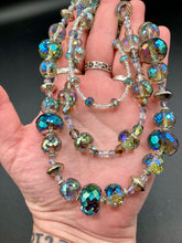 Load image into Gallery viewer, This beautiful necklace features shimmery, rich aqua blue and silver tones glass beads. Its three strands consist primarily of faceted rondelle shaped beads, along with a variety of lighter blue and silver beads, resulting in a unique multicolored look. The perfect statement piece, this elegant necklace will drape beautifully across your neck, adding a vibrant hue to any Spring outfit. Measurements: Necklace is 18” in length