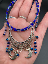 Load image into Gallery viewer, This stylish choker necklace showcases a large half moon pendant, adorned with glass beads and small, dangling crescent moon charms. Its eye-catching hues, of blue and silver, are complemented with delicate tints of purple and pink. Boasting an accentuated look and ample motion, this piece is sure to impress. Measurements: Necklace is 16 1/2”adjustable up to 18"