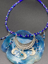 Load image into Gallery viewer, This stylish choker necklace showcases a large half moon pendant, adorned with glass beads and small, dangling crescent moon charms. Its eye-catching hues, of blue and silver, are complemented with delicate tints of purple and pink. Boasting an accentuated look and ample motion, this piece is sure to impress. Measurements: Necklace is 16 1/2”adjustable up to 18"