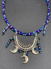 Load image into Gallery viewer, This stylish choker necklace showcases a large half moon pendant, adorned with glass beads and small, dangling crescent moon charms. Its eye-catching hues, of blue and silver, are complemented with delicate tints of purple and pink. Boasting an accentuated look and ample motion, this piece is sure to impress. Measurements: Necklace is 16 1/2”adjustable up to 18"