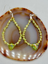 Load image into Gallery viewer, These natural peridot chips earrings feature a gold glass beading on their hoops, creating an eye-catching light green tone. A pressed glass leaf charm is also included, boasting an iridescent shimmer finish with subtle hints of gold, purple, blue, and pink. Measurements: 2 1/2" length