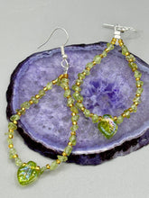 Load image into Gallery viewer, These natural peridot chips earrings feature a gold glass beading on their hoops, creating an eye-catching light green tone. A pressed glass leaf charm is also included, boasting an iridescent shimmer finish with subtle hints of gold, purple, blue, and pink. Measurements: 2 1/2" length