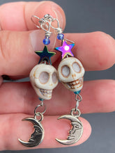 Load image into Gallery viewer, Galaxy Cosmos Stardust Howlite Skull Bead Earrings - star shaped rainbow hematite beads and smiling crescent moons. These pair of earrings have a lot of movement and shimmer for that witchy vibe. You can dress these up or down, it will definitely give your outfit a unique look. Measurements: 2 ” in length