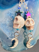 Load image into Gallery viewer, Galaxy Cosmos Stardust Howlite Skull Bead Earrings - star shaped rainbow hematite beads and smiling crescent moons. These pair of earrings have a lot of movement and shimmer for that witchy vibe. You can dress these up or down, it will definitely give your outfit a unique look. Measurements: 2 ” in length