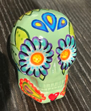 Load image into Gallery viewer, Inspired by nature, this ceramic skull statuette is full of vibrant color and intricate details. The primary color is soft, light periwinkle blue with Multi-color floral motifs that are painted across the skull, along with hearts and leaves and lively colorful accents around the entire skull.