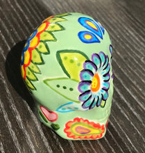 Load image into Gallery viewer, Inspired by nature, this ceramic skull statuette is full of vibrant color and intricate details. The primary color is soft, light periwinkle blue with Multi-color floral motifs that are painted across the skull, along with hearts and leaves and lively colorful accents around the entire skull.