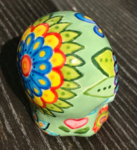 Load image into Gallery viewer, Inspired by nature, this ceramic skull statuette is full of vibrant color and intricate details. The primary color is soft, light periwinkle blue with Multi-color floral motifs that are painted across the skull, along with hearts and leaves and lively colorful accents around the entire skull.