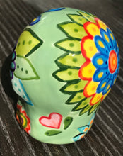 Load image into Gallery viewer, Inspired by nature, this ceramic skull statuette is full of vibrant color and intricate details. The primary color is soft, light periwinkle blue with Multi-color floral motifs that are painted across the skull, along with hearts and leaves and lively colorful accents around the entire skull.