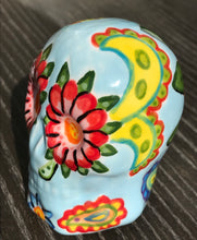 Load image into Gallery viewer, Inspired by nature, this ceramic skull statuette is full of vibrant color and intricate details. The primary color is soft, light periwinkle blue with Multi-color floral motifs that are painted across the skull, along with hearts and leaves and lively colorful accents around the entire skull.