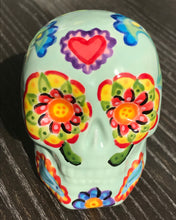 Load image into Gallery viewer, This Mini Light Green Dia De Los Muertos Hand Painted Ceramic Sugar Skull is a unique and vibrant piece of art. Its soft mint green base is filled with beautiful, detailed motifs of nature, such as colorful floral designs, hearts, and leaves. Perfect as an altar decoration or to add a fun, gothic touch to any space. Measurements: H 2 3/4” x W 2” x D 2”