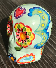 Load image into Gallery viewer, This Mini Light Green Dia De Los Muertos Hand Painted Ceramic Sugar Skull is a unique and vibrant piece of art. Its soft mint green base is filled with beautiful, detailed motifs of nature, such as colorful floral designs, hearts, and leaves. Perfect as an altar decoration or to add a fun, gothic touch to any space. Measurements: H 2 3/4” x W 2” x D 2”