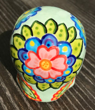 Load image into Gallery viewer, This Mini Light Green Dia De Los Muertos Hand Painted Ceramic Sugar Skull is a unique and vibrant piece of art. Its soft mint green base is filled with beautiful, detailed motifs of nature, such as colorful floral designs, hearts, and leaves. Perfect as an altar decoration or to add a fun, gothic touch to any space. Measurements: H 2 3/4” x W 2” x D 2”
