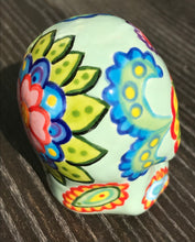 Load image into Gallery viewer, Inspired by nature, this ceramic skull statuette is full of vibrant color and intricate details. The primary color is soft pastel green with Multi-color floral motifs that are painted across the skull, along with hearts and leaves and lively colorful accents around the entire skull.