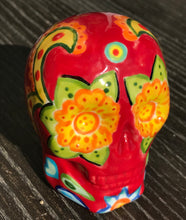Load image into Gallery viewer, This ceramic skull statuette is a stunning piece of art inspired by nature. Its vibrant red hue is decorated with multi-color floral motifs, hearts, leaves and colorful accents, creating a beautiful piece of hand-painted, Day of the Dead-themed art. Measurements: H 2 3/4” x W 2” x D 2”