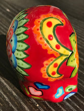 Load image into Gallery viewer, This ceramic skull statuette is a stunning piece of art inspired by nature. Its vibrant red hue is decorated with multi-color floral motifs, hearts, leaves and colorful accents, creating a beautiful piece of hand-painted, Day of the Dead-themed art. Measurements: H 2 3/4” x W 2” x D 2”