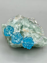 Load image into Gallery viewer, This light blue pressed glass floral bracelet is a sophisticated addition to any summer look. Its iridescent shimmer finish adds a classy touch to its intricate metal wire and lobster claw clasp. Perfect for any nature-inspired wardrobe. Measurements: Bracelet: 8" in length