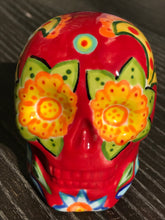 Load image into Gallery viewer, This ceramic skull statuette is a stunning piece of art inspired by nature. Its vibrant red hue is decorated with multi-color floral motifs, hearts, leaves and colorful accents, creating a beautiful piece of hand-painted, Day of the Dead-themed art. Measurements: H 2 3/4” x W 2” x D 2”